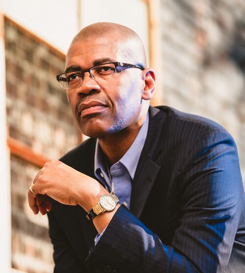 A photo of Dr. Reuben A. Buford May. He is looking pensively to the side of the camera.