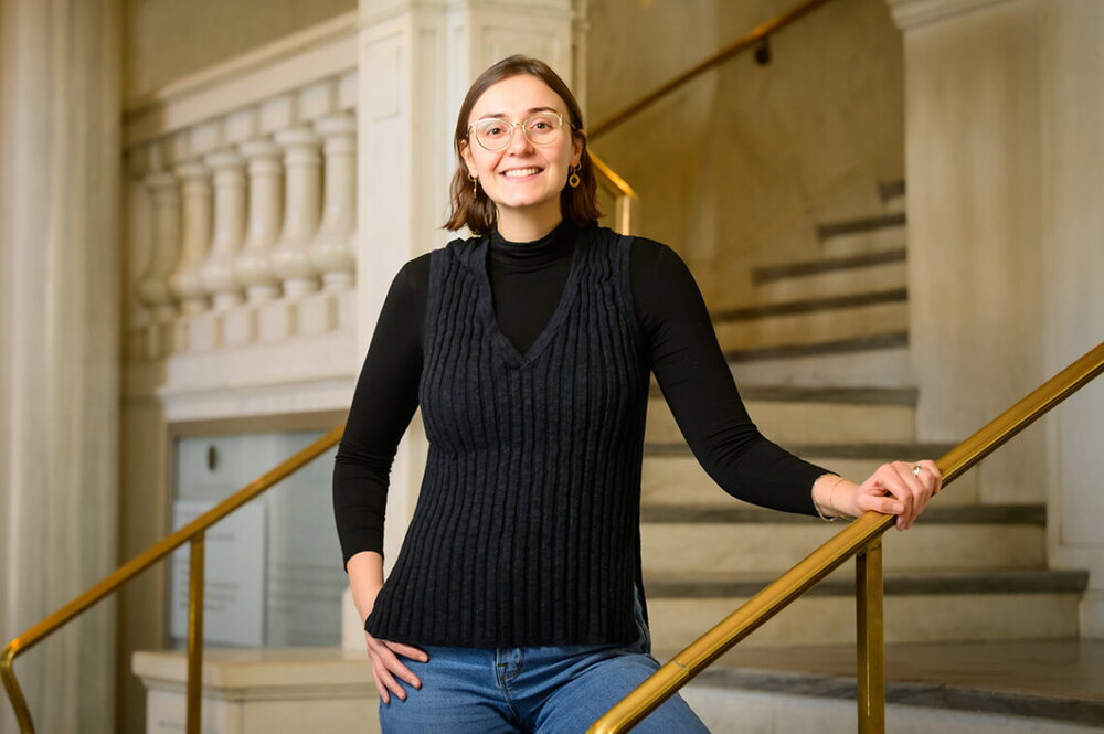 Christina Kamis smiles at the viewer; she is standing in front of a marble staircase.