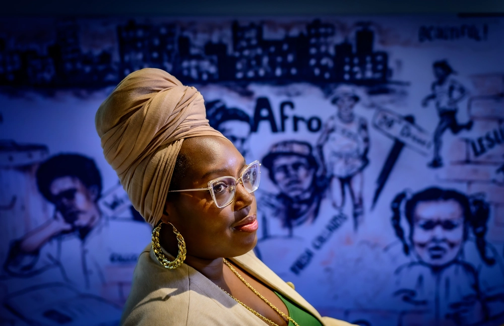A photo of Dr. Brittney Miles. She wears a light tan head wrap and blazer