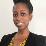 Nikel A. Bailey smiles at the camera. She wears a black blazer and yellow shirt and has her hair in a loc bun atop her head.