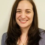 Loren Henderson smiling at the camera. She has long dark hair and wears a gray suit.